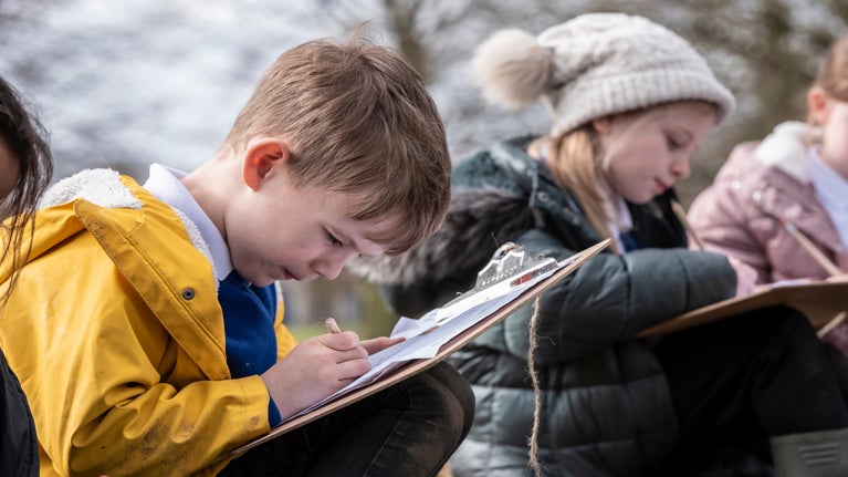 Two primary school children on their 'Eco Walk' in the park, filling in a worksheet on their clipboards.